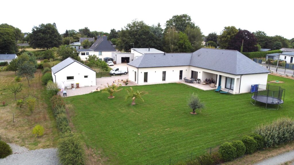 Maison moderne avec toiture ardoise, grand jardin vert et dépendances attenantes dans un environnement résidentiel calme.