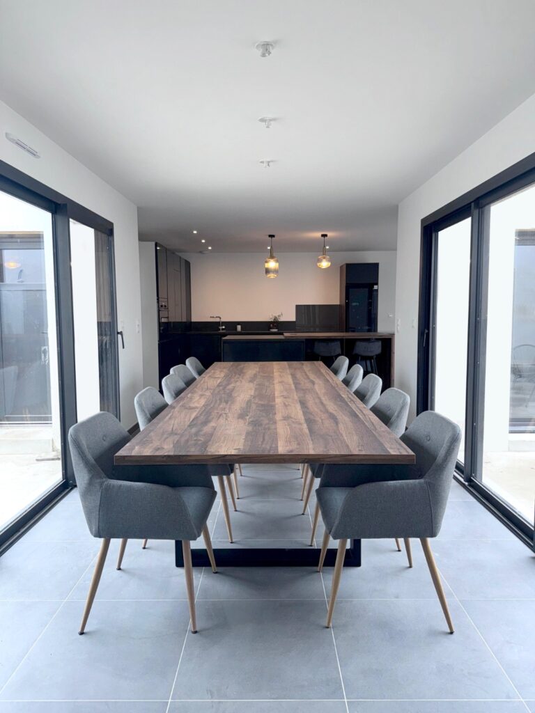 Cuisine moderne avec une table en bois et des chaises grises. Sur l'image on aperçois de grandes baies vitrées.